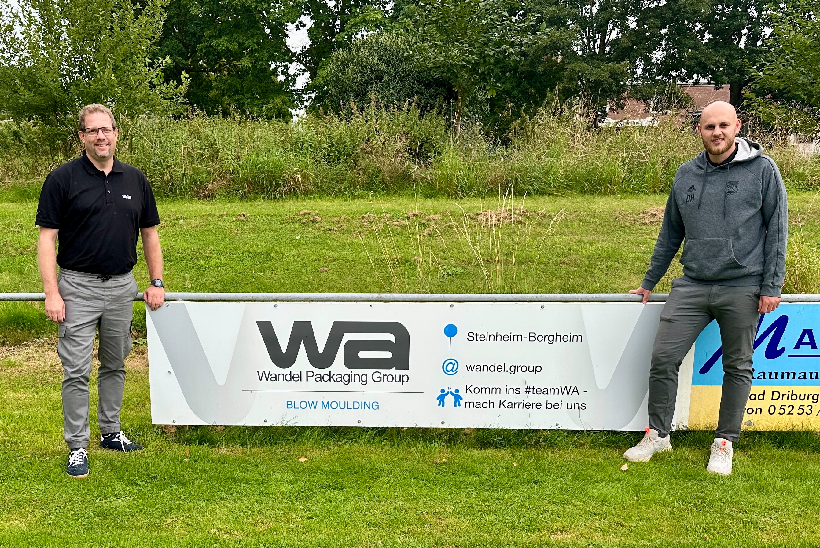 Bande auf dem Fußballplatz mit zwei Vertretern von WPG und dem Fußballverein